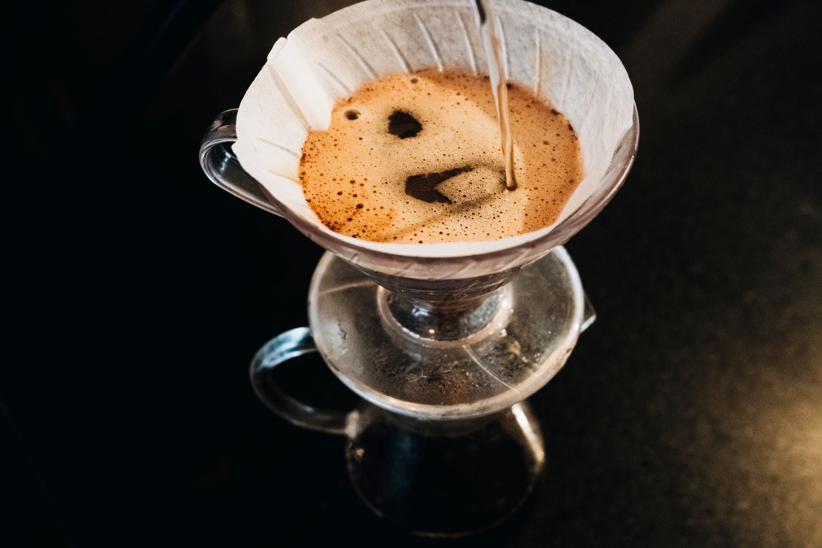 Looking down into a paper filter as hot water blooms freshly ground coffee on a glass dripper