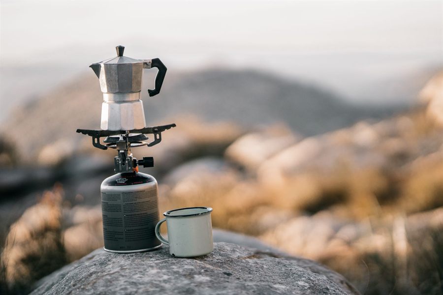 Moka pot on a camping stove with an enamel mug