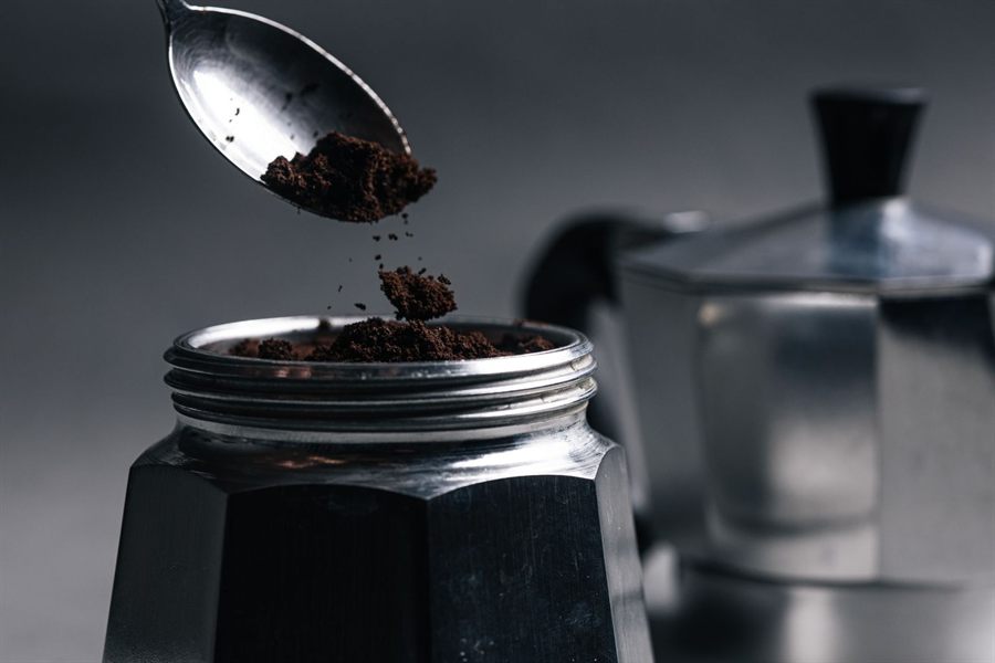Spoon tipping ground coffee into a moka pot basket