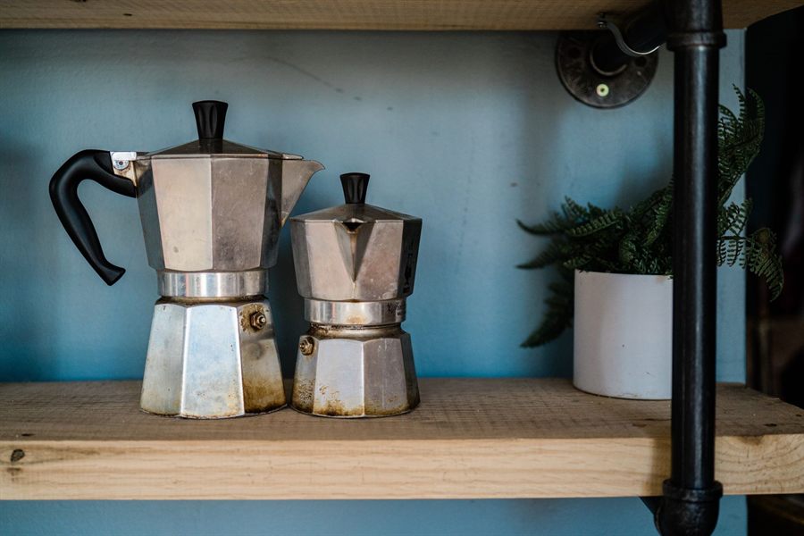 Two aluminum moka pots on a kitchen shelf