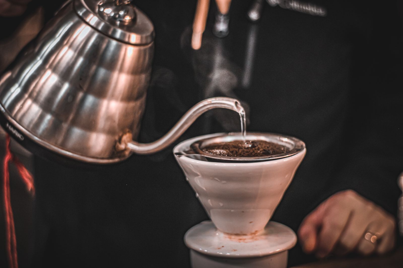Gooseneck kettle pouring a thin stream of water into a white cone pour-over dripper