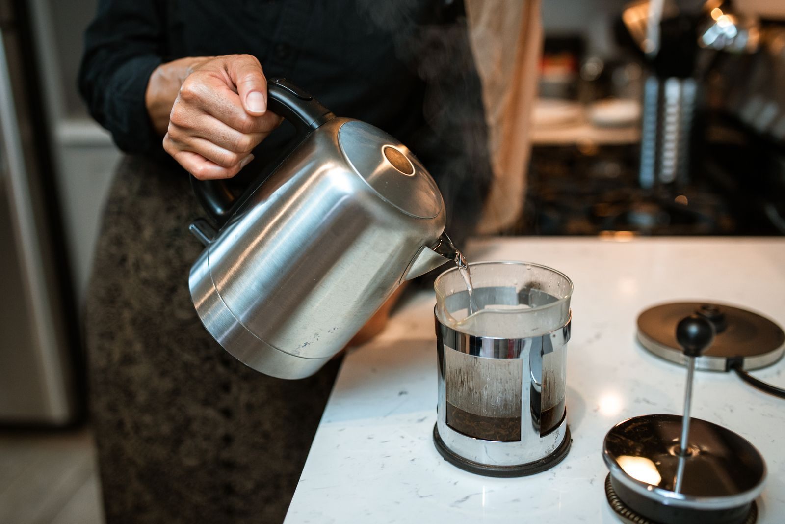 How to brew coffee in a French press: pouring hot water from a steel kettle onto coffee grounds in a glass press